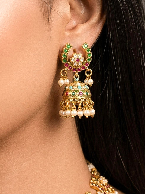 Close-up of a woman wearing an ornate traditional Navratan jadau gold jewellery set and jadau earrings with navratan color stone and Pearls. Woman wearing a premium Jadau artificial jewelry set for reception night. Mehendi function outfit styled with a lightweight Jadau necklace.