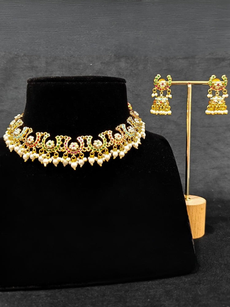 Close-up of an ornate traditional Navratan jadau gold jewellery set and jadau earrings with navratan color stone and Pearls. Festive celebration look featuring a Jadau artificial necklace. Elegant look featuring a luxury Jadau artificial jewelry set.