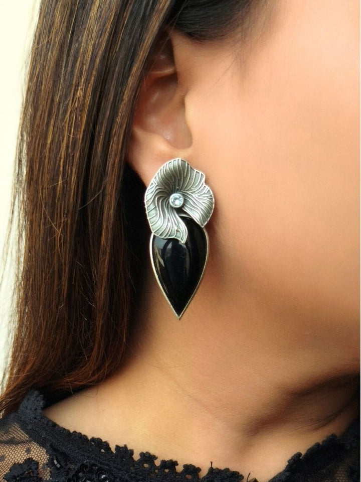 A close-up shows a woman wearing Habiscus Black Earrings—large alloy earrings with silver floral detailing with an american diamond in the center along with a black stone drop—against her ear and brown hair, making them ideal to complement a wedding ceremony dress.