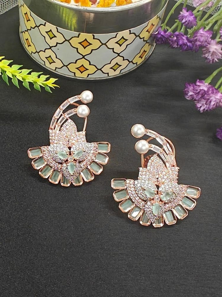 The Mint Green Hansini Earrings feature an ornate floral design with American diamonds and pearls, displayed on a black surface near a decorative container and red flowers—perfect for pairing with your favorite cocktail gown.