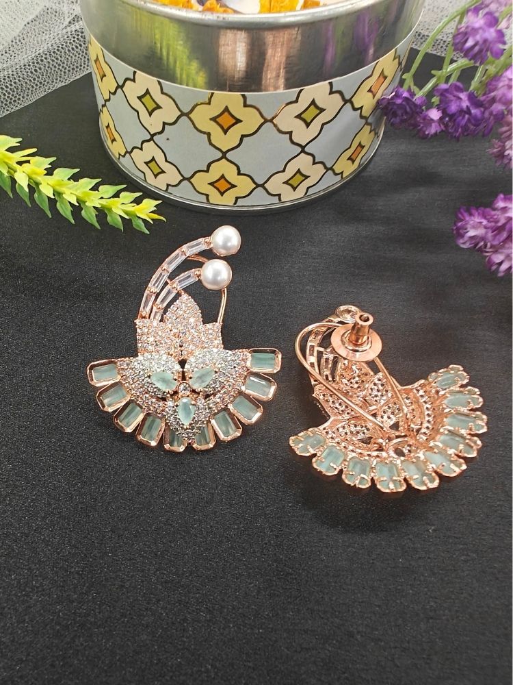 The Mint Green Hansini Earrings feature an ornate floral design with American diamonds and pearls, displayed on a black surface near a decorative container and red flowers—perfect for pairing with your favorite cocktail gown.