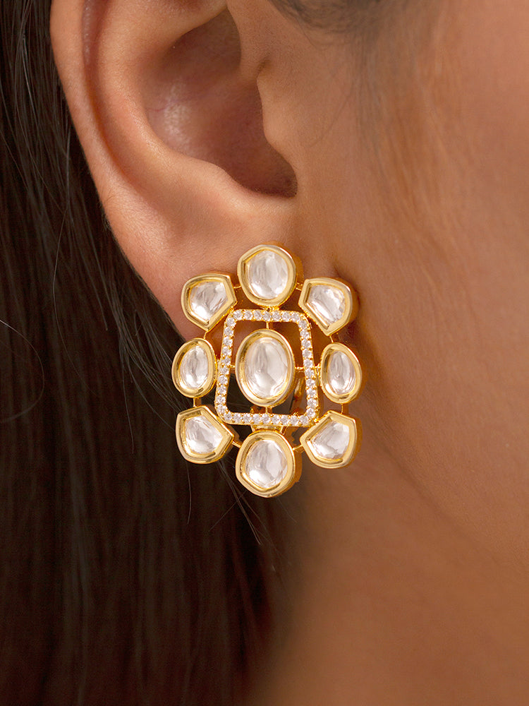 A Harley necklace set with a gold-colored chain and a pair of matching earrings, adorned with white and yellow diamonds, displayed on a dark background with a cup of tea and yellow flowers in the background.

