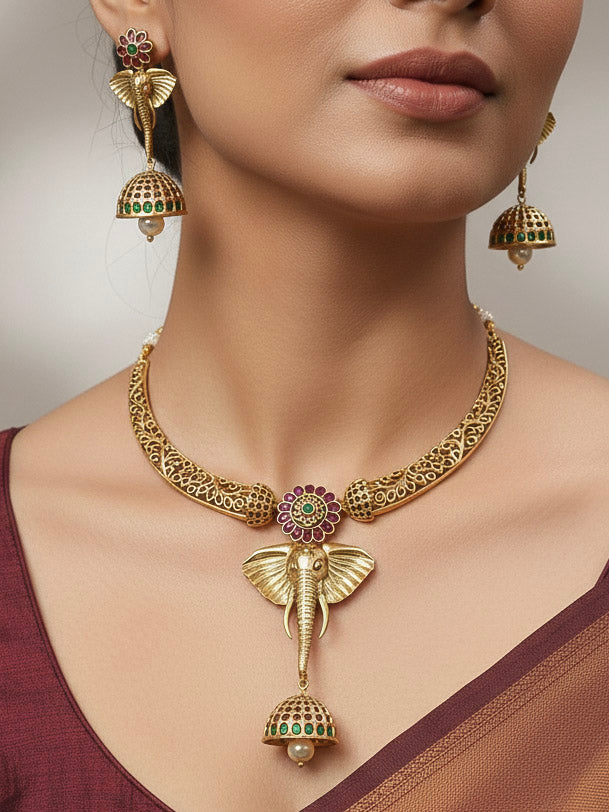 A woman wearing the Hastika Hasli Necklace Set featuring a traditional gold Collar hasli necklace and matching earrings with Goddess Ganesh in the middle, along with pink and green colored stones and golden elephants, paired with a Saree—ideal party jewelry for any festive occasion. Festive Diwali look completed with a traditional temple necklace set.