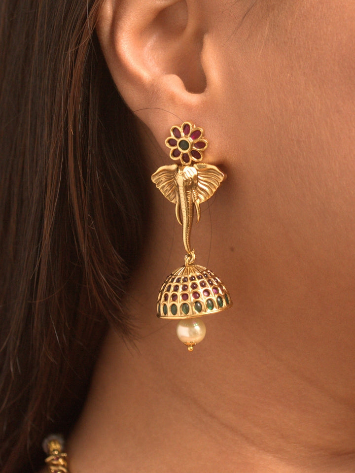 A woman wearing the Hastika Hasli Necklace Set featuring a traditional gold Collar hasli necklace and matching earrings with Goddess Ganesh in the middle, along with pink and green colored stones and golden elephants, paired with a Saree—ideal party jewelry for any festive occasion. Festive Diwali look completed with a traditional temple necklace set.