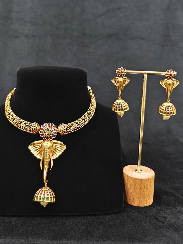 The Hastika Hasli Necklace Set featuring a traditional gold Collar hasli necklace and matching earrings with Goddess Ganesh in the middle, along with pink and green colored stones and golden elephants. Ideal party jewelry for any festive occasion. Festive Diwali look completed with a traditional temple necklace set.