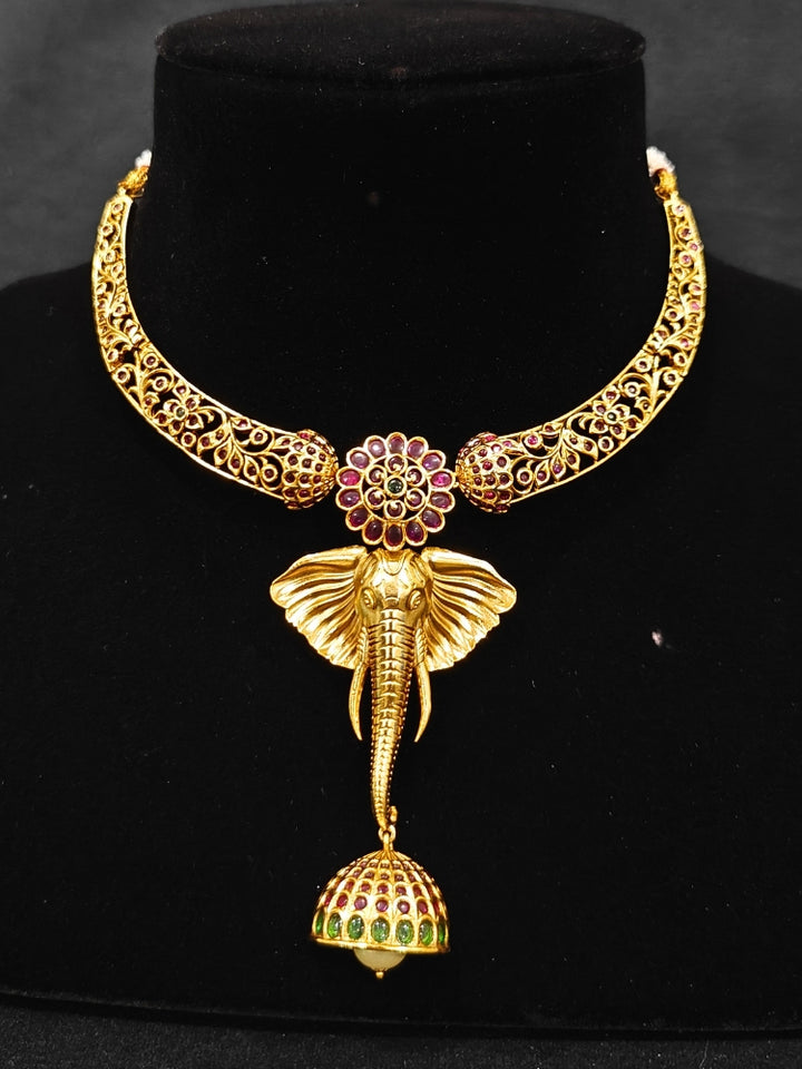 The Hastika Hasli Necklace Set featuring a traditional gold Collar hasli necklace and matching earrings with Goddess Ganesh in the middle, along with pink and green colored stones and golden elephants. Ideal party jewelry for any festive occasion. Festive Diwali look completed with a traditional temple necklace set.