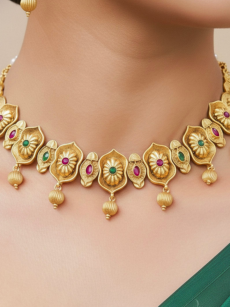 Close-up of a woman wearing an ornate traditional (Bright Gold Polish) Collar jewellery set and earrings with Pink and Green Colored Stone. Woman pairing a traditional Colored Stone necklace with a silk saree. Festive Diwali look enhanced with an imitation Colored Stone Necklace Set.