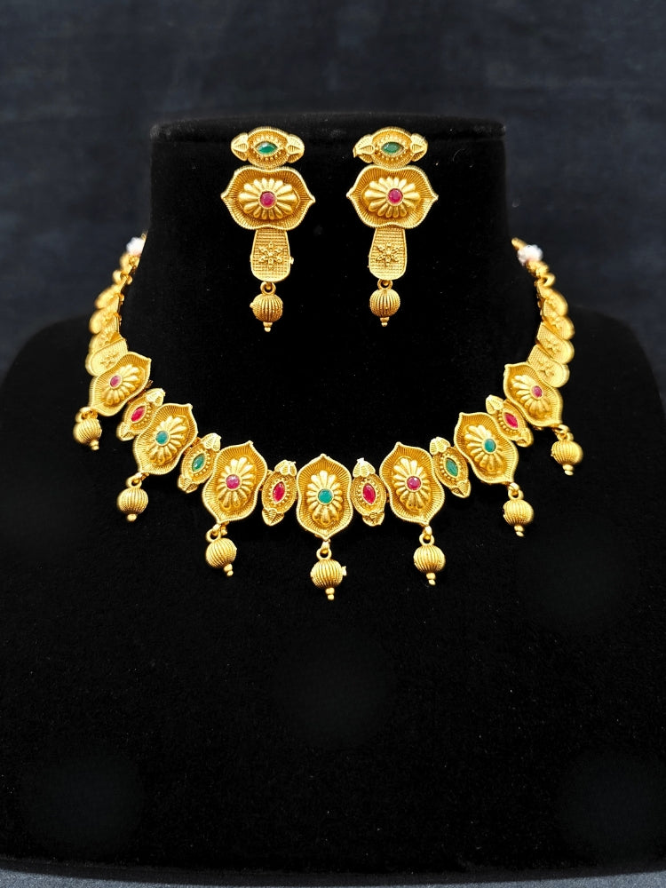 Close-up of an ornate traditional (Bright Gold Polish) Collar jewellery set and earrings with Pink and Green Colored Stone. Woman pairing a traditional Colored Stone necklace with a silk saree. Festive Diwali look enhanced with an imitation Colored Stone Necklace Set.
