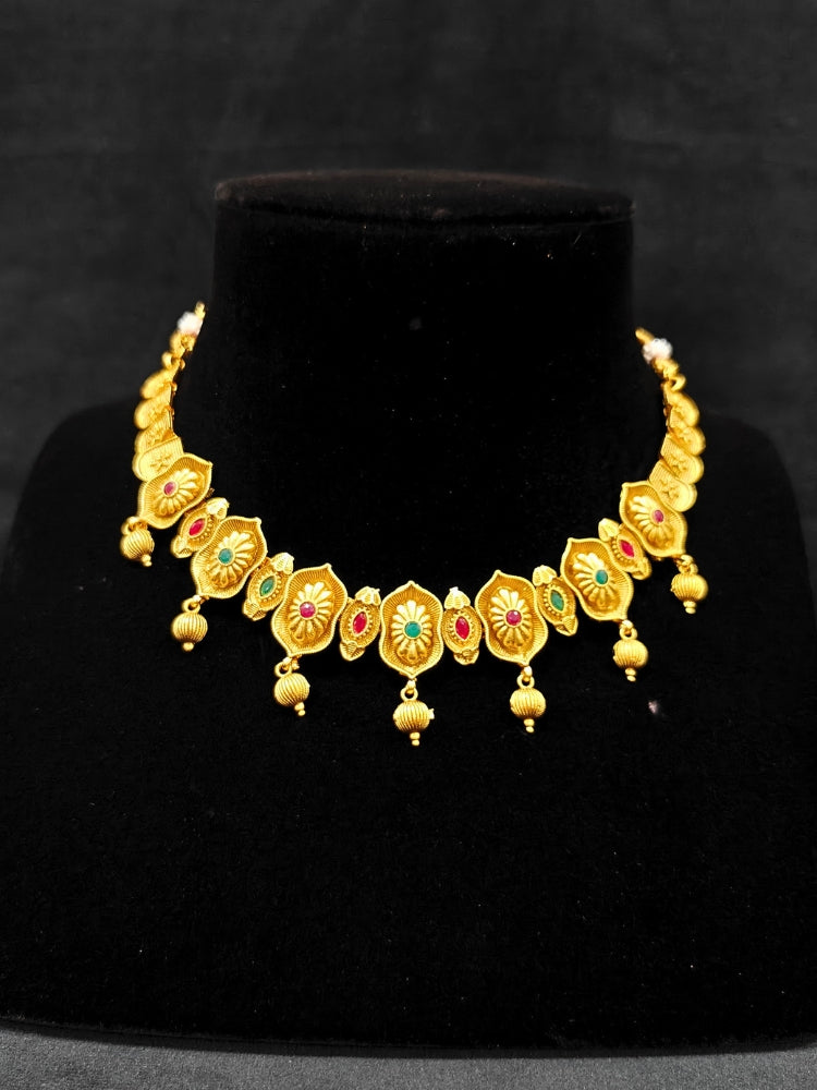 Close-up of an ornate traditional (Bright Gold Polish) Collar jewellery set and earrings with Pink and Green Colored Stone. Woman pairing a traditional Colored Stone necklace with a silk saree. Festive Diwali look enhanced with an imitation Colored Stone Necklace Set.