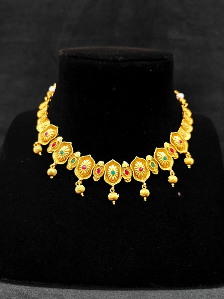 Close-up of an ornate traditional (Bright Gold Polish) Collar jewellery set and earrings with Pink and Green Colored Stone. Woman pairing a traditional Colored Stone necklace with a silk saree. Festive Diwali look enhanced with an imitation Colored Stone Necklace Set.