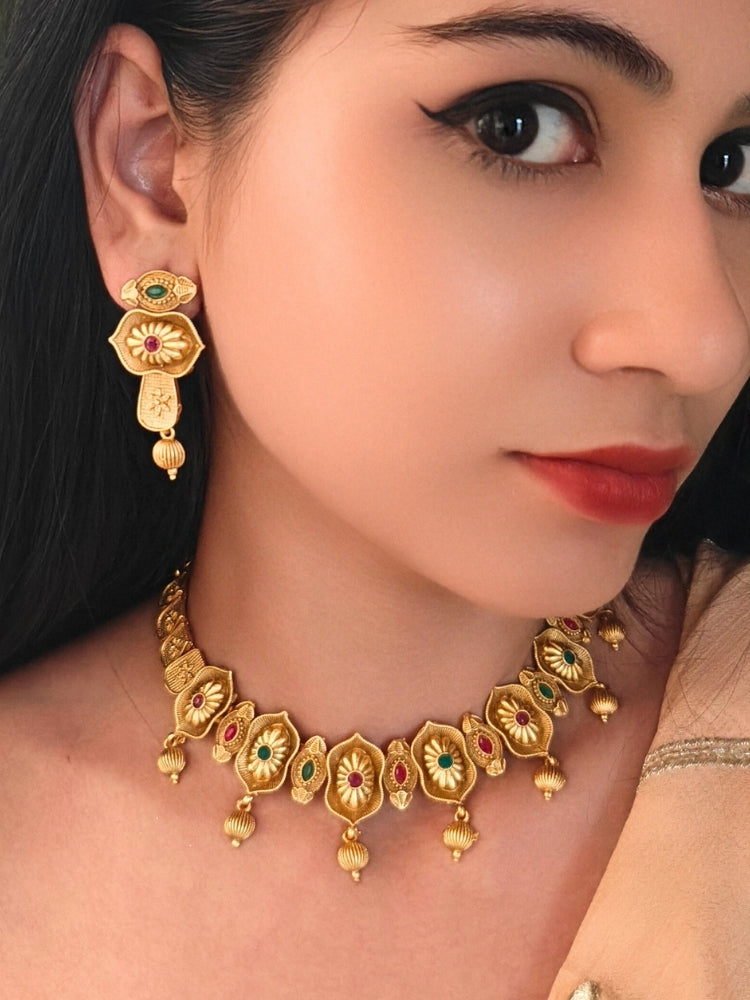 Close-up of a women wearing an ornate traditional (Bright Gold Polish) Collar jewellery set and earrings with Pink and Green Colored Stone. Woman pairing a traditional Colored Stone necklace with a silk saree. Festive Diwali look enhanced with an imitation Colored Stone Necklace Set.