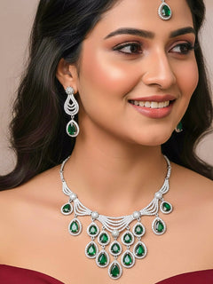 Close-up of a woman wearing an ornate Western Green Silver Polish Collar Diamond jewellery set and earrings and maangtikka with American Diamond and Colored Stones. Bride-to-be styled in a premium American diamond artificial necklace for her reception party. Woman styling a statement American diamond necklace with an off-shoulder gown for a reception.
