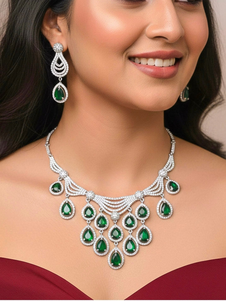 Close-up of a woman wearing an ornate Western Green Silver Polish Collar Diamond jewellery set and earrings and maangtikka with American Diamond and Colored Stones. Bride-to-be styled in a premium American diamond artificial necklace for her reception party. Woman styling a statement American diamond necklace with an off-shoulder gown for a reception.