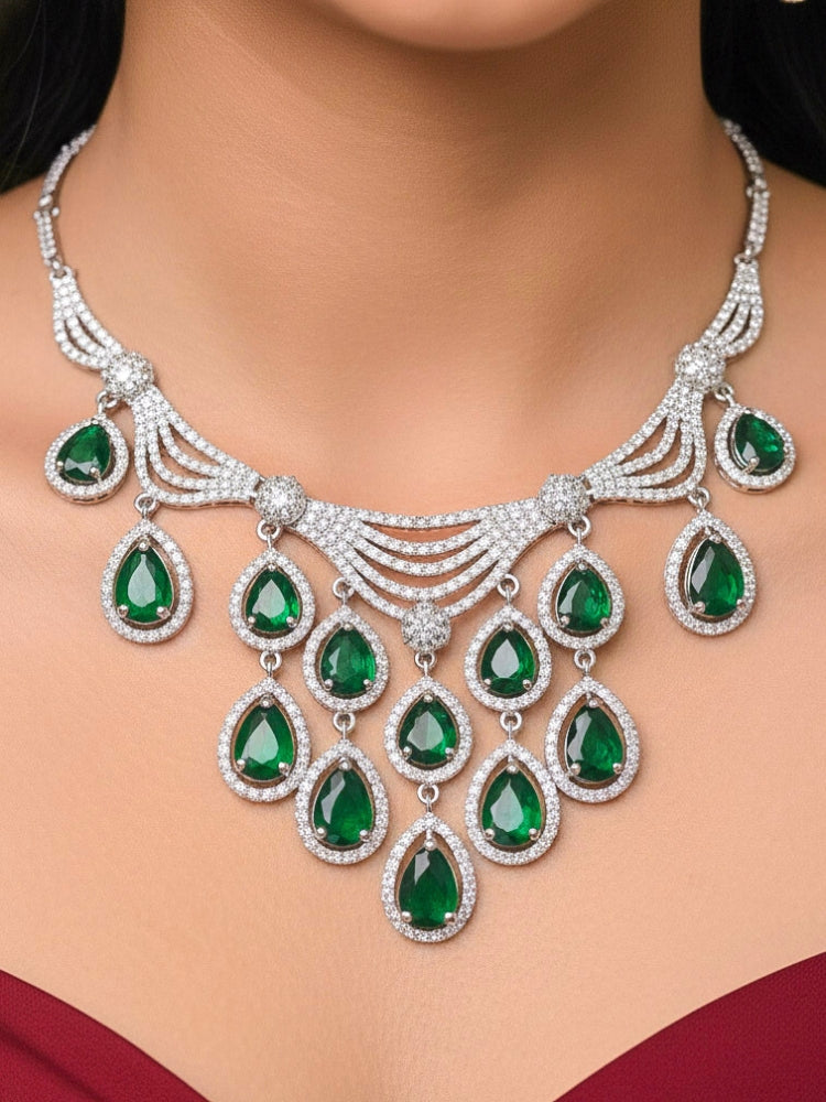 Close-up of a woman wearing an ornate Western Green Silver Polish Collar Diamond jewellery set and earrings and maangtikka with American Diamond and Colored Stones. Bride-to-be styled in a premium American diamond artificial necklace for her reception party. Woman styling a statement American diamond necklace with an off-shoulder gown for a reception.