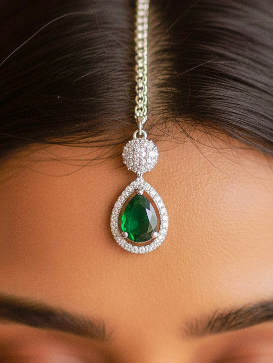 Close-up of a woman wearing an ornate Western Green Silver Polish Collar Diamond jewellery set and earrings and maangtikka with American Diamond and Colored Stones. Bride-to-be styled in a premium American diamond artificial necklace for her reception party. Woman styling a statement American diamond necklace with an off-shoulder gown for a reception.