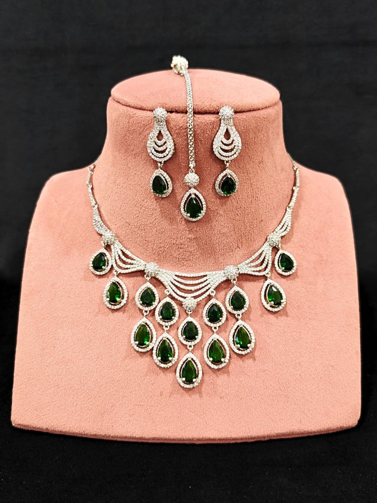 Close-up of an ornate Western Green Silver Polish Collar Diamond jewellery set and earrings and maangtikka with American Diamond and Colored Stones. A premium American diamond artificial necklace for reception party. A statement American diamond necklace with an off-shoulder gown for a reception.