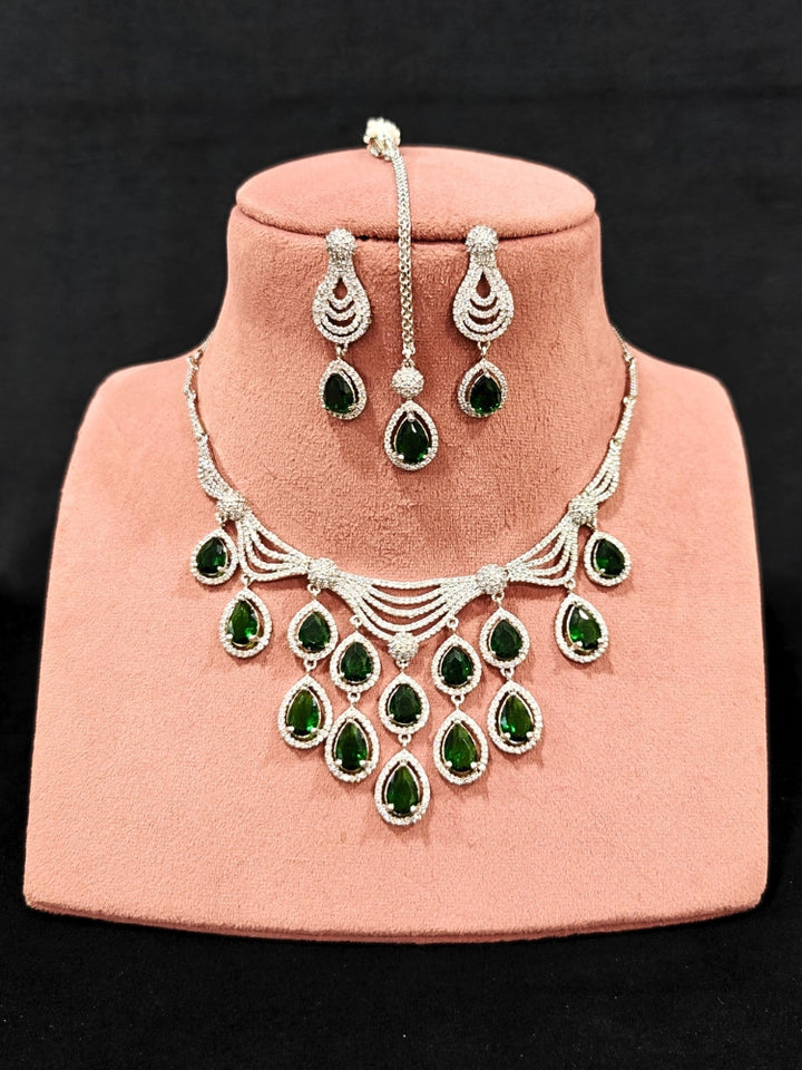 Close-up of an ornate Western Green Silver Polish Collar Diamond jewellery set and earrings and maangtikka with American Diamond and Colored Stones. A premium American diamond artificial necklace for reception party. A statement American diamond necklace with an off-shoulder gown for a reception.