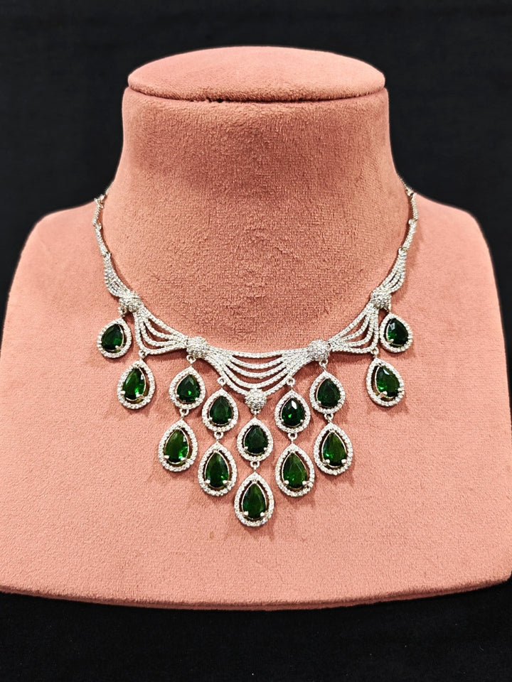Close-up of an ornate Western Green Silver Polish Collar Diamond jewellery set and earrings and maangtikka with American Diamond and Colored Stones. A premium American diamond artificial necklace for reception party. A statement American diamond necklace with an off-shoulder gown for a reception.