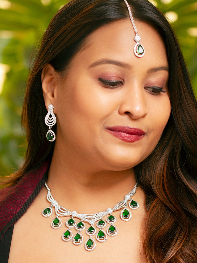 A bride-to-be wearing an exquisite artificial diamond necklace with green colored stone and matching earrings and maangtikka, designed for the perfect engagement look. This stunning artificial diamond jewelry set offers luxury and sophistication while being an affordable alternative to natural diamonds.