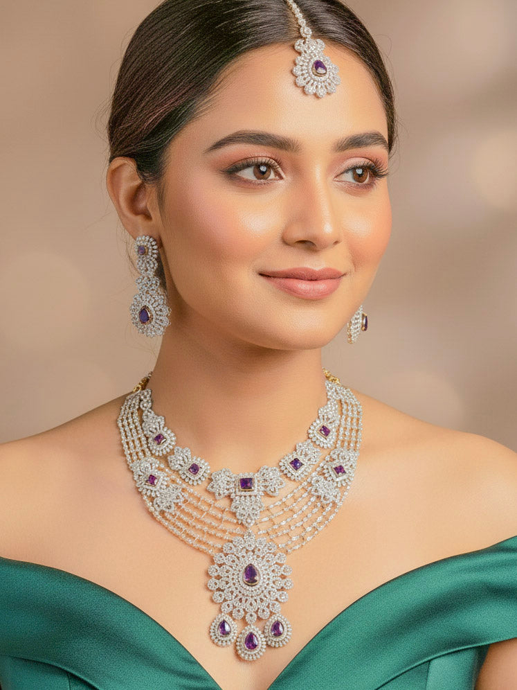 A beautiful woman wearing an elegant artificial diamond necklace with purple colored stone and matching earrings and maangtikka. This premium artificial diamond jewelry set is perfect for special occasions, from Indian weddings to engagement parties, offering sophisticated glamour without the high price tag.