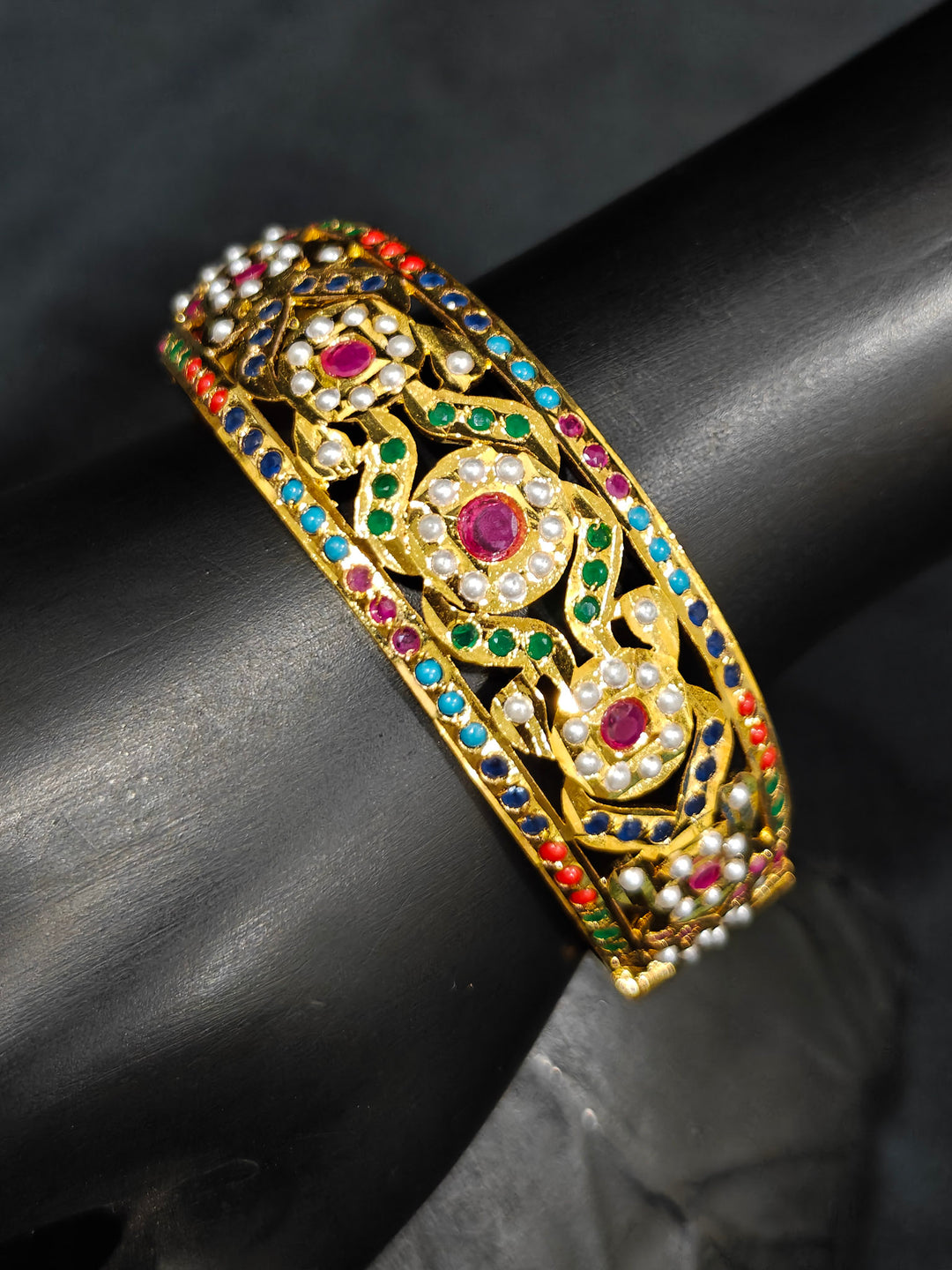 Close-up of an ornate traditional Navratan jadau gold Bracelet with matched Ring with pearls and Color Stone. A premium artificial Jadau bracelet with Ring for wedding celebrations. Close-up of a high-quality imitation Jadau bracelet with Ring for festive wear.