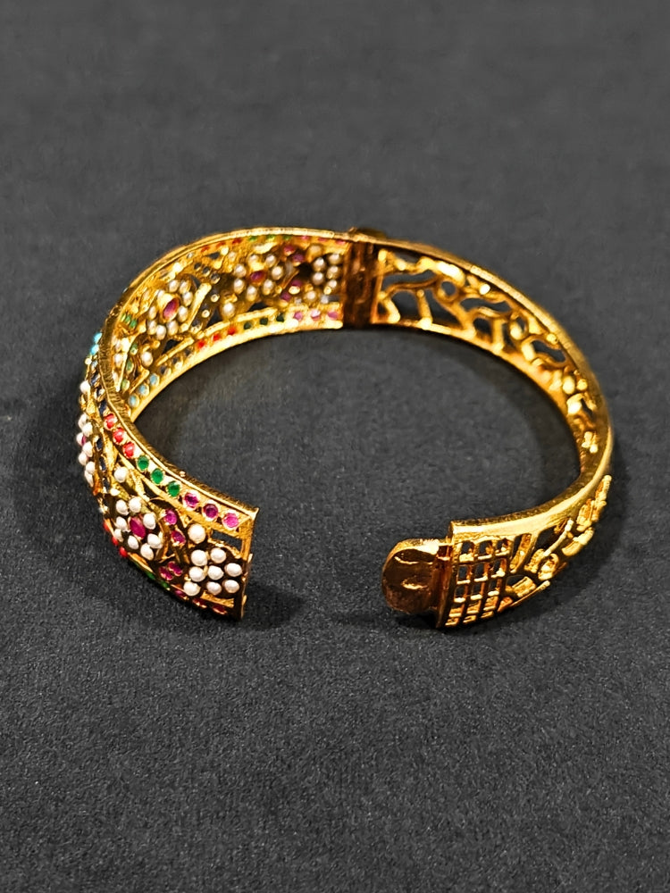 Close-up of an ornate traditional Navratan jadau gold Bracelet with matched Ring with pearls and Color Stone. A premium artificial Jadau bracelet with Ring for wedding celebrations. Close-up of a high-quality imitation Jadau bracelet with Ring for festive wear.