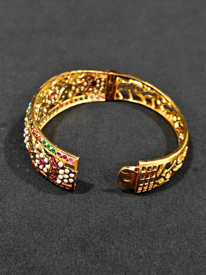 Close-up of an ornate traditional Navratan jadau gold Bracelet with matched Ring with pearls and Color Stone. A premium artificial Jadau bracelet with Ring for wedding celebrations. Close-up of a high-quality imitation Jadau bracelet with Ring for festive wear.