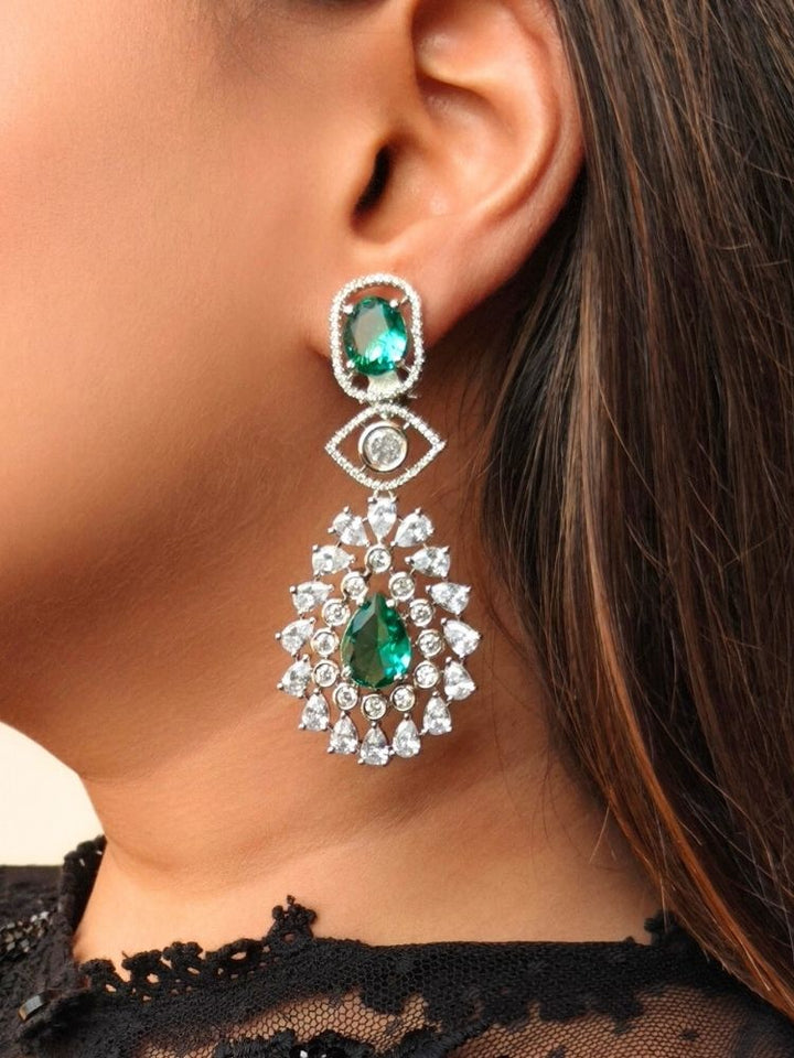 A close-up of a woman’s ear wearing Ira Earrings—statement green brass earrings with American Diamonds and an intricate teardrop design. Her dark hair and part of a black lace top are visible in the background.