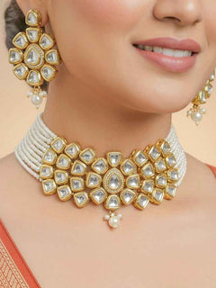 Close-up of a woman wearing an ornate traditional (Gold Polish) White Kundan  Choker jewellery set and earrings with Kundan and Pearls. Bride wearing a royal Kundan artificial necklace for wedding rituals. Close-up of detailed Kundan stones in artificial wedding jewelry. 