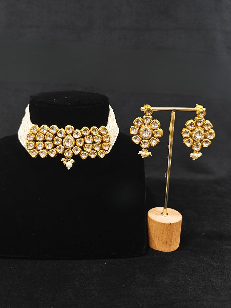 Close-up of an ornate traditional (Gold Polish) White Kundan  Choker jewellery set and earrings with Kundan and Pearls. Bride wearing a royal Kundan artificial necklace for wedding rituals. Close-up of detailed Kundan stones in artificial wedding jewelry. 