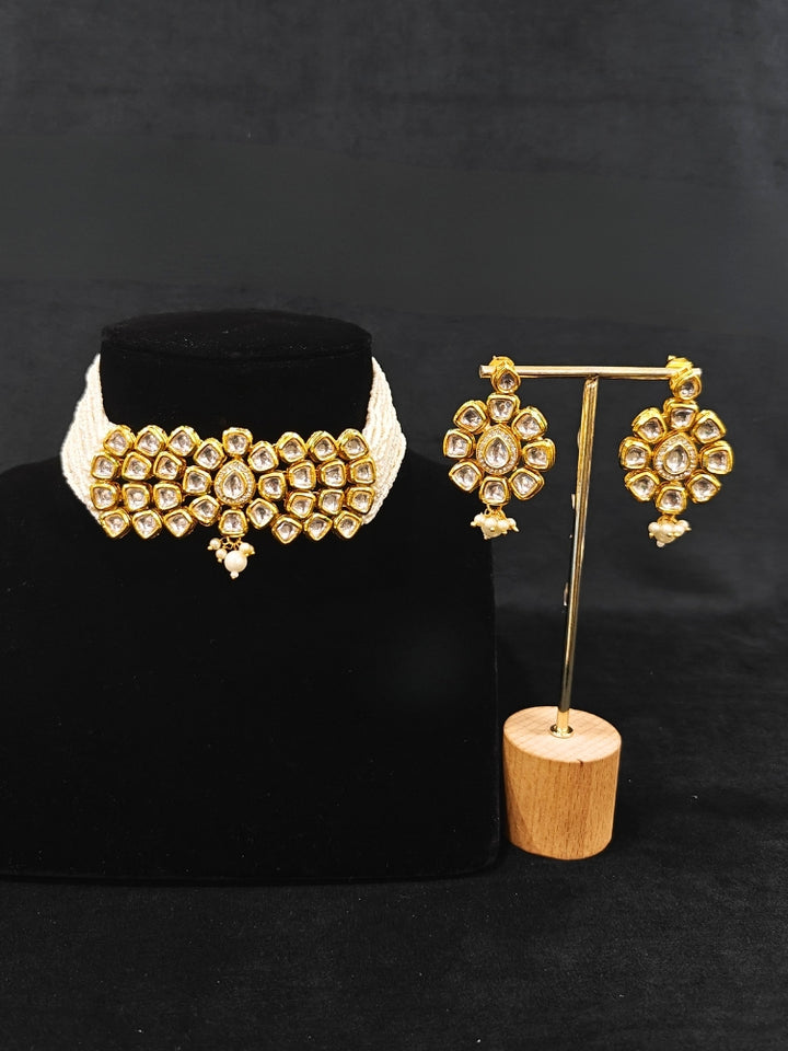 Close-up of an ornate traditional (Gold Polish) White Kundan  Choker jewellery set and earrings with Kundan and Pearls. Bride wearing a royal Kundan artificial necklace for wedding rituals. Close-up of detailed Kundan stones in artificial wedding jewelry. 