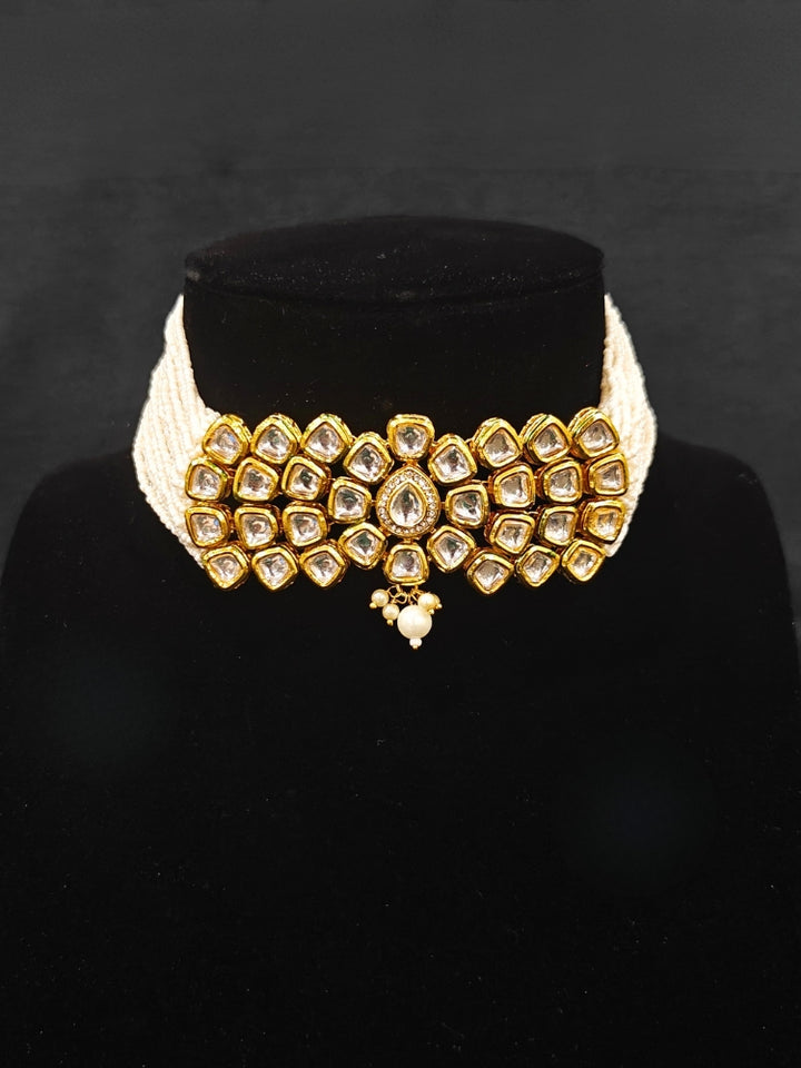 Close-up of an ornate traditional (Gold Polish) White Kundan  Choker jewellery set and earrings with Kundan and Pearls. Bride wearing a royal Kundan artificial necklace for wedding rituals. Close-up of detailed Kundan stones in artificial wedding jewelry. 