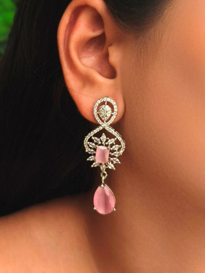 Close-up of a woman wearing an ornate Western (Silver Polish) Pink Diamond Earrings with American Diamond and Pink Colored Stones. Woman wearing statement artificial American Diamond earrings for a wedding guest look in India. Reception-ready look completed with statement artificial jewelry American Diamond earrings.