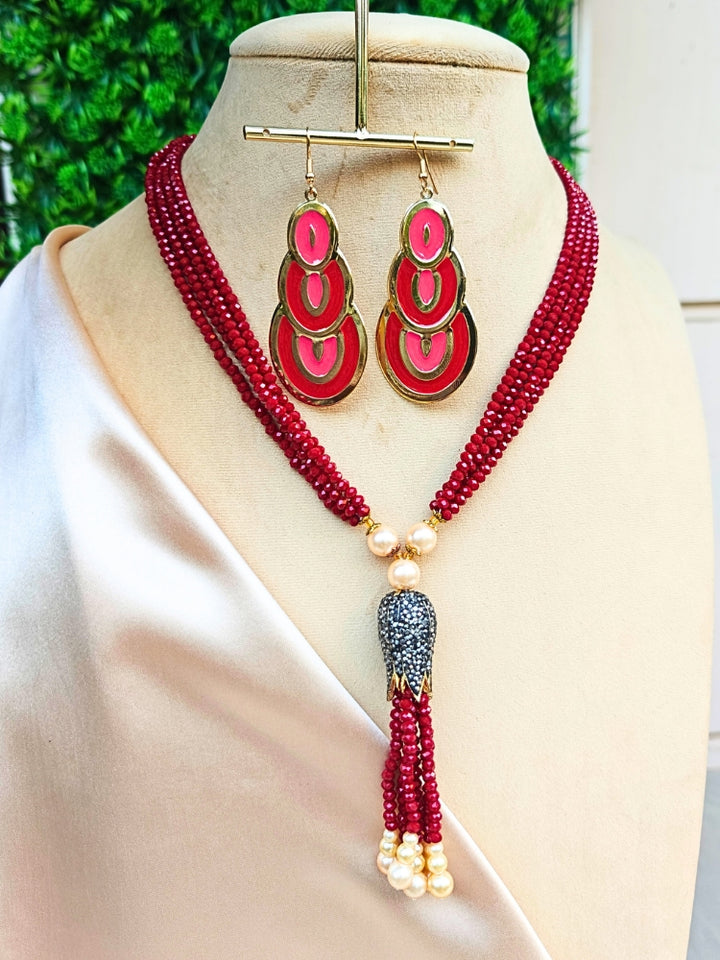 A mannequin showcases the Jade Red Necklace Set—featuring a layered Red necklace with crystal beads and gold accents, plus matching turquoise and gold dangle earrings—against a soft floral backdrop.