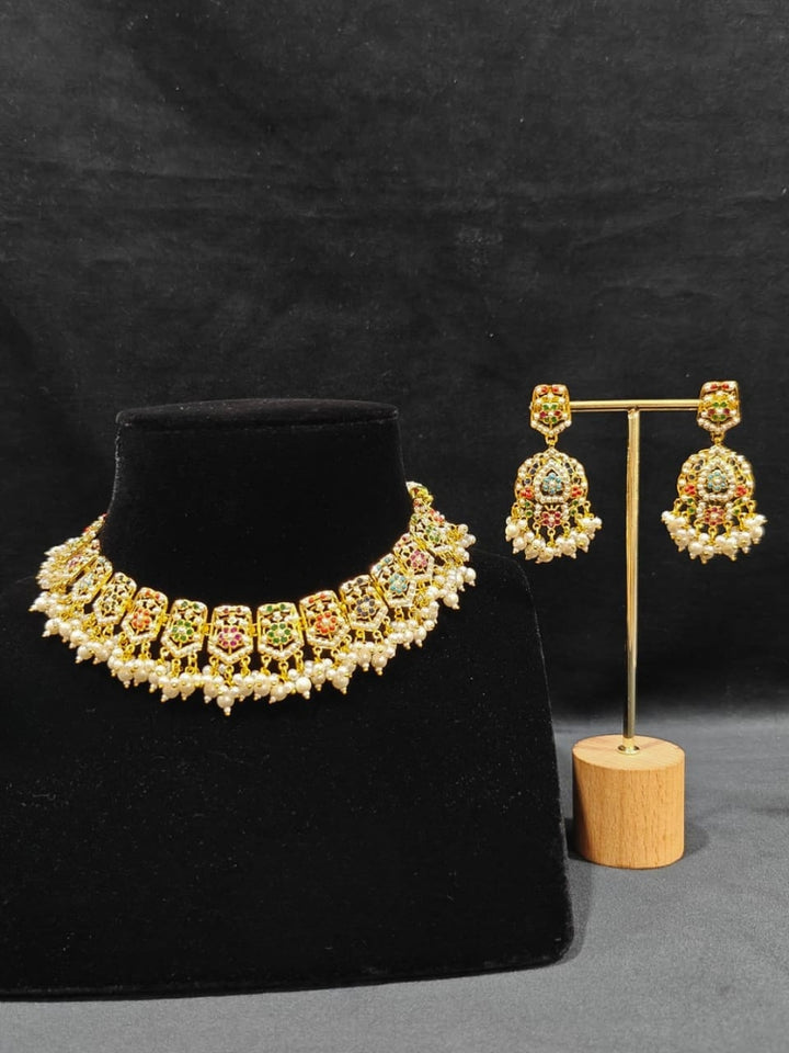 Close-up of an ornate traditional collar Navratan jadau gold jewellery set and jadau earrings with pearls and Navratan gemstones. Festive celebration look featuring a Jadau artificial necklace. Styling inspiration with a premium Jadau imitation necklace.