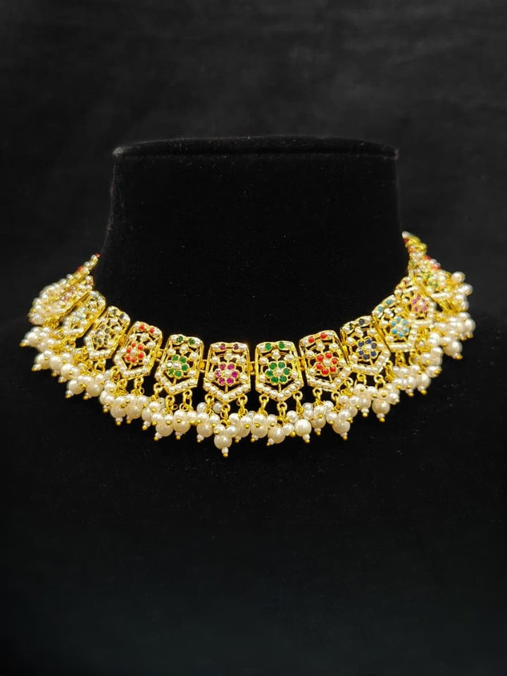 Close-up of an ornate traditional collar Navratan jadau gold jewellery set and jadau earrings with pearls and Navratan gemstones. Festive celebration look featuring a Jadau artificial necklace. Styling inspiration with a premium Jadau imitation necklace.