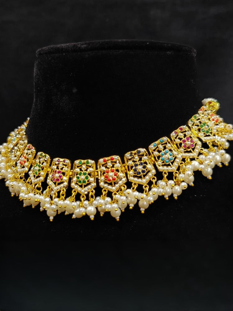 Close-up of an ornate traditional collar Navratan jadau gold jewellery set and jadau earrings with pearls and Navratan gemstones. Festive celebration look featuring a Jadau artificial necklace. Styling inspiration with a premium Jadau imitation necklace.