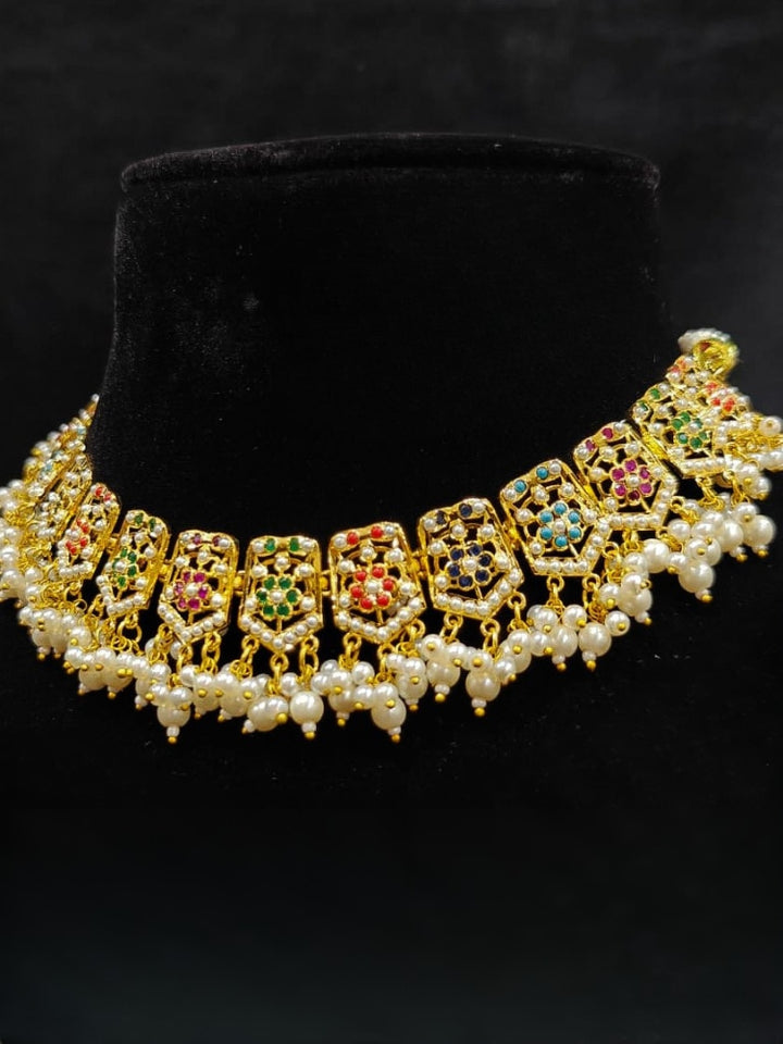 Close-up of an ornate traditional collar Navratan jadau gold jewellery set and jadau earrings with pearls and Navratan gemstones. Festive celebration look featuring a Jadau artificial necklace. Styling inspiration with a premium Jadau imitation necklace.