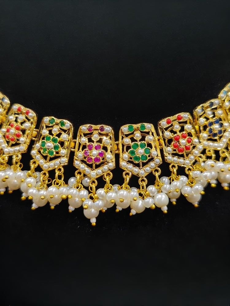 Close-up of an ornate traditional collar Navratan jadau gold jewellery set and jadau earrings with pearls and Navratan gemstones. Festive celebration look featuring a Jadau artificial necklace. Styling inspiration with a premium Jadau imitation necklace.