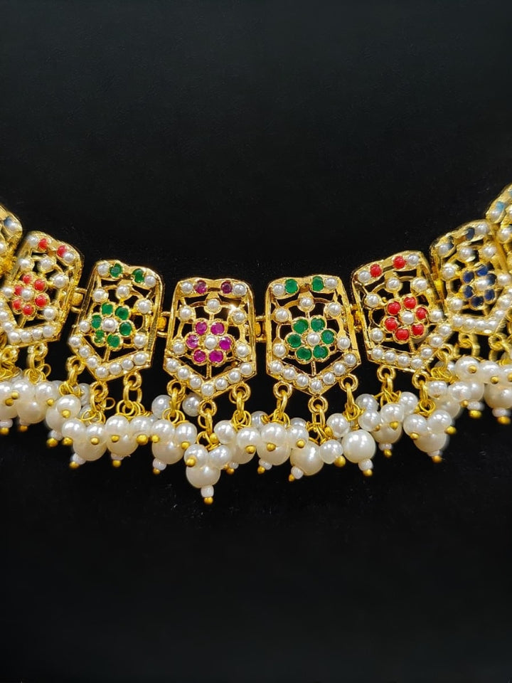 Close-up of an ornate traditional collar Navratan jadau gold jewellery set and jadau earrings with pearls and Navratan gemstones. Festive celebration look featuring a Jadau artificial necklace. Styling inspiration with a premium Jadau imitation necklace.