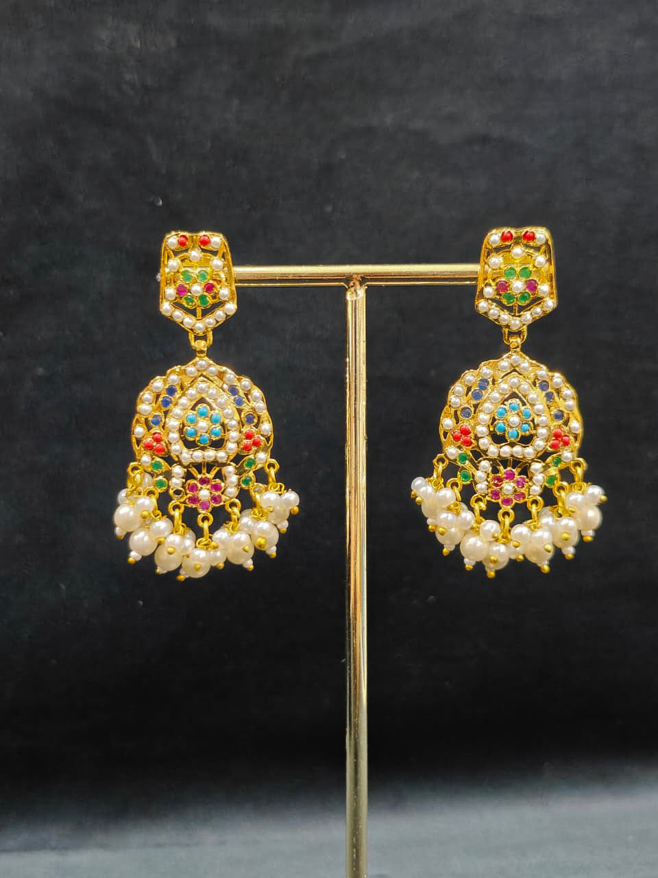 Close-up of an ornate traditional collar Navratan jadau gold jewellery set and jadau earrings with pearls and Navratan gemstones. Festive celebration look featuring a Jadau artificial necklace. Styling inspiration with a premium Jadau imitation necklace.