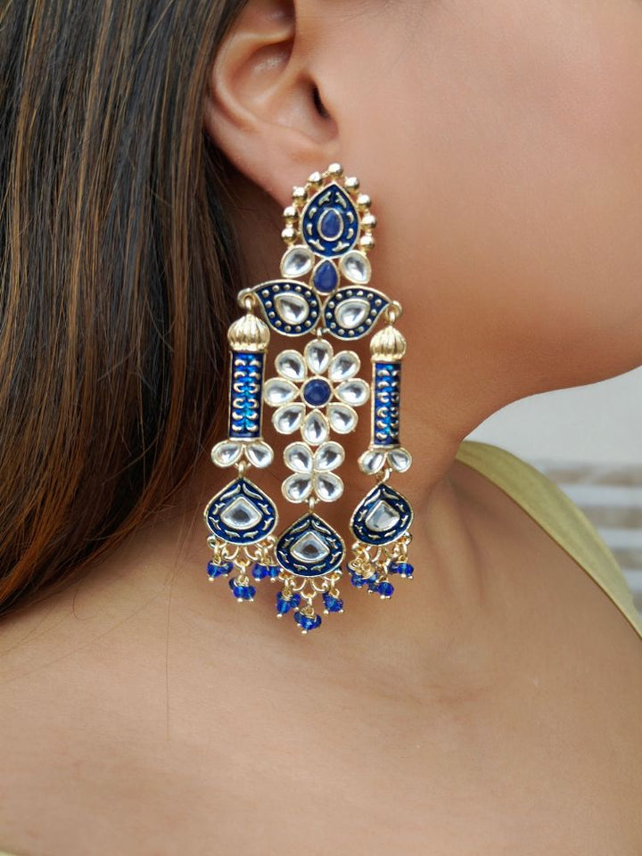 A close-up of a womans ear wearing Jasmine Blue Earrings—large, ornate Meenakari long earrings with Blue and gold accents, white kundan stones, pearl bead hangings, and intricate floral and geometric patterns.