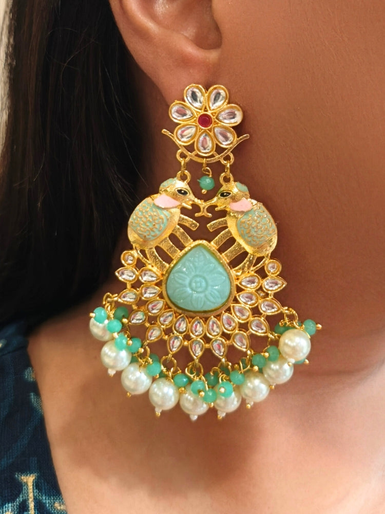 A close-up of a womans ear adorned with Jaya Green Long Earrings, featuring two bird designs, floral motifs, intricate Kundan work, and dangling pearls.