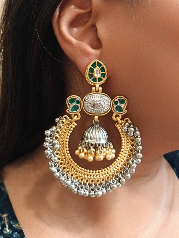 A close-up of a womans ear adorned with Jhanak Green Earrings, featuring ornate green stones, gold, brass, and silver details, intricate circlular patterns, small beads, pearls, and a small jhumki at the centre. Oxidized earrings, german silver earrings, navratri earrings. 