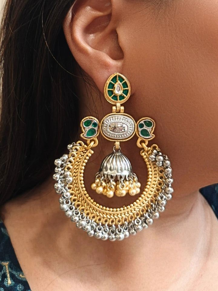A close-up of a womans ear adorned with Jhanak Green Earrings, featuring ornate green stones, gold, brass, and silver details, intricate circlular patterns, small beads, pearls, and a small jhumki at the centre. Oxidized earrings, german silver earrings, navratri earrings. 