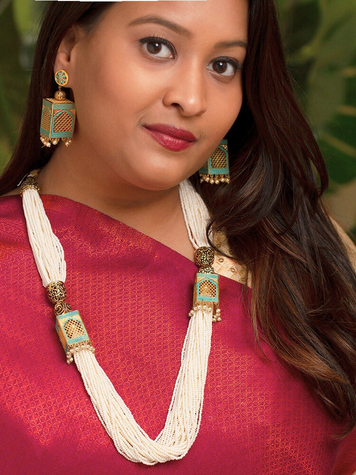 Close-up of a woman wearing an ornate traditional Mint Green Rajwadi gold Long jewellery set and earrings  with  Pearls and Meenakari. Festive Diwali outfit enhanced with a Rajwadi artificial necklace. Woman pairing a Rajwadi necklace with a red saree. Close-up of enamel work in Meenakari artificial wedding jewelry.