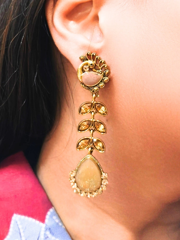 A close-up of a womans ear wearing Kajal Brown Earrings—large, ornate earrings with brass and American diamond accents, leaf-shaped segments, and a teardrop pendant. She pairs them with a Brown patterned top—ideal Wedding Ceremony Jewelry. Oxidized earrings, german silver earrings, navratri earrings. 