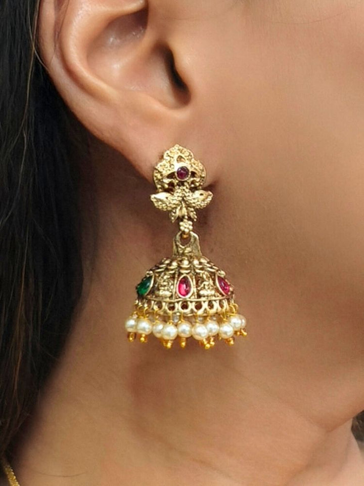A woman wears a maroon and green sari with gold South-Indian jewelry, including the Kamakshi Temple Necklace Set featuring intricate traditional designs and deity motifs.