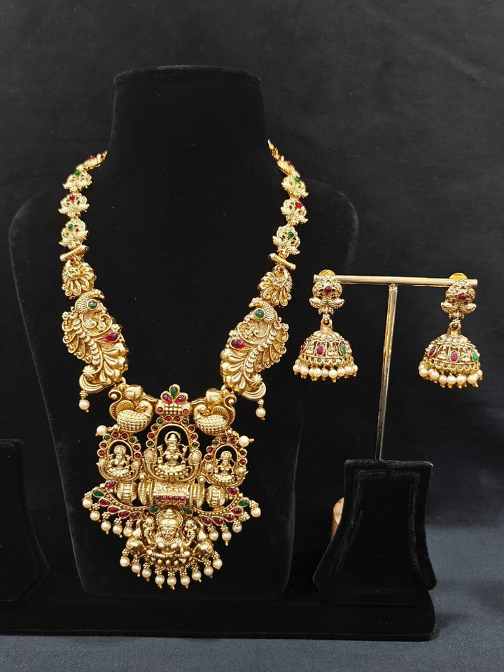 The Kamakshi Temple Necklace Set featuring a traditional gold Long necklace and matching earrings with Goddess Laxmi in the middle, along with pink and green colored stones and pearls, Perfect Temple necklace set for weddings and festivals.