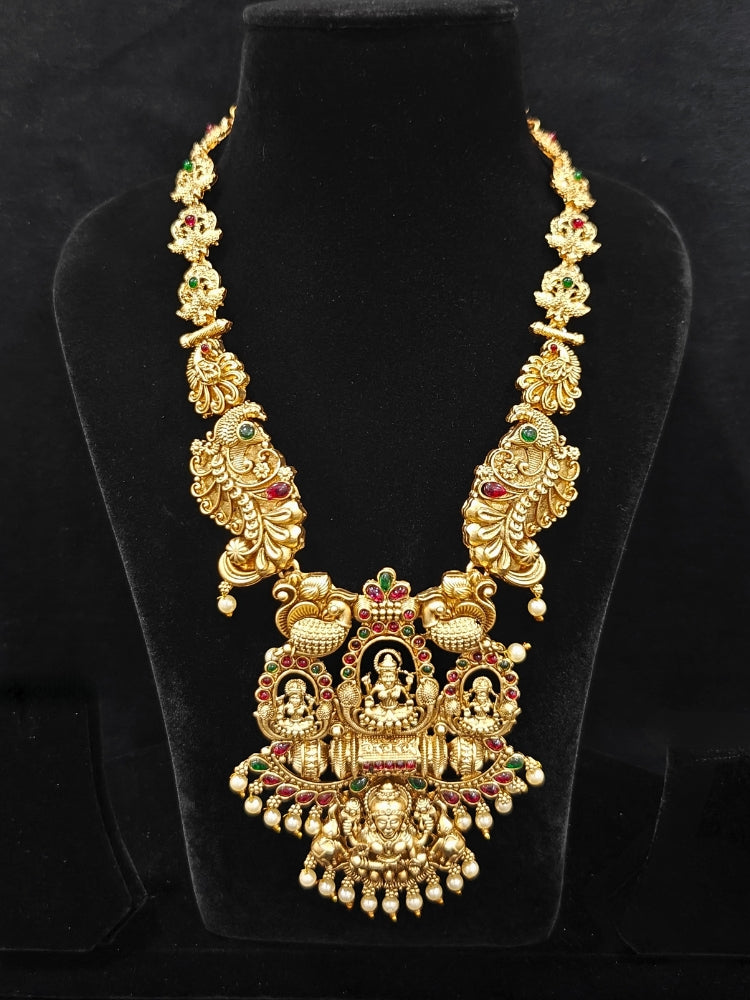 The Kamakshi Temple Necklace Set featuring a traditional gold Long necklace and matching earrings with Goddess Laxmi in the middle, along with pink and green colored stones and pearls, Perfect Temple necklace set for weddings and festivals.